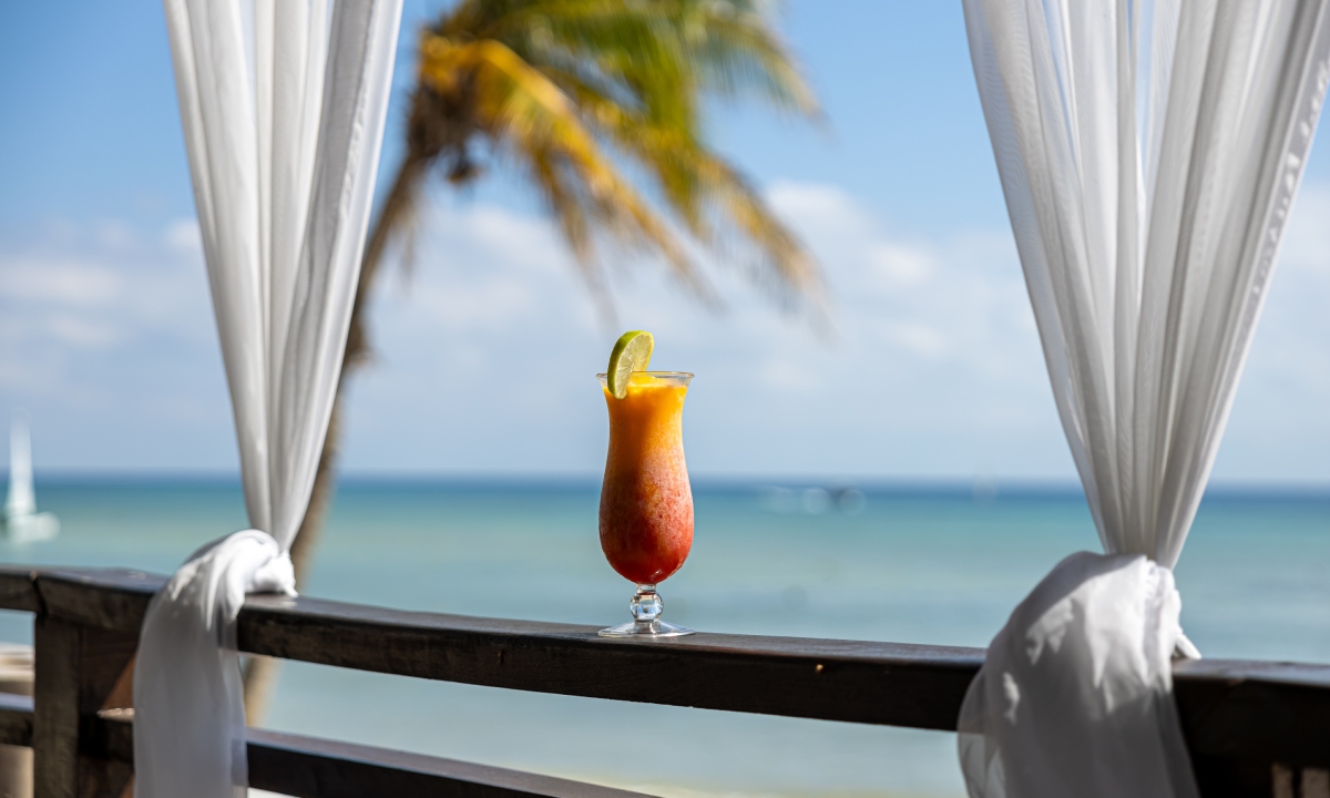 A cocktail resting on a railing with the sea in the background