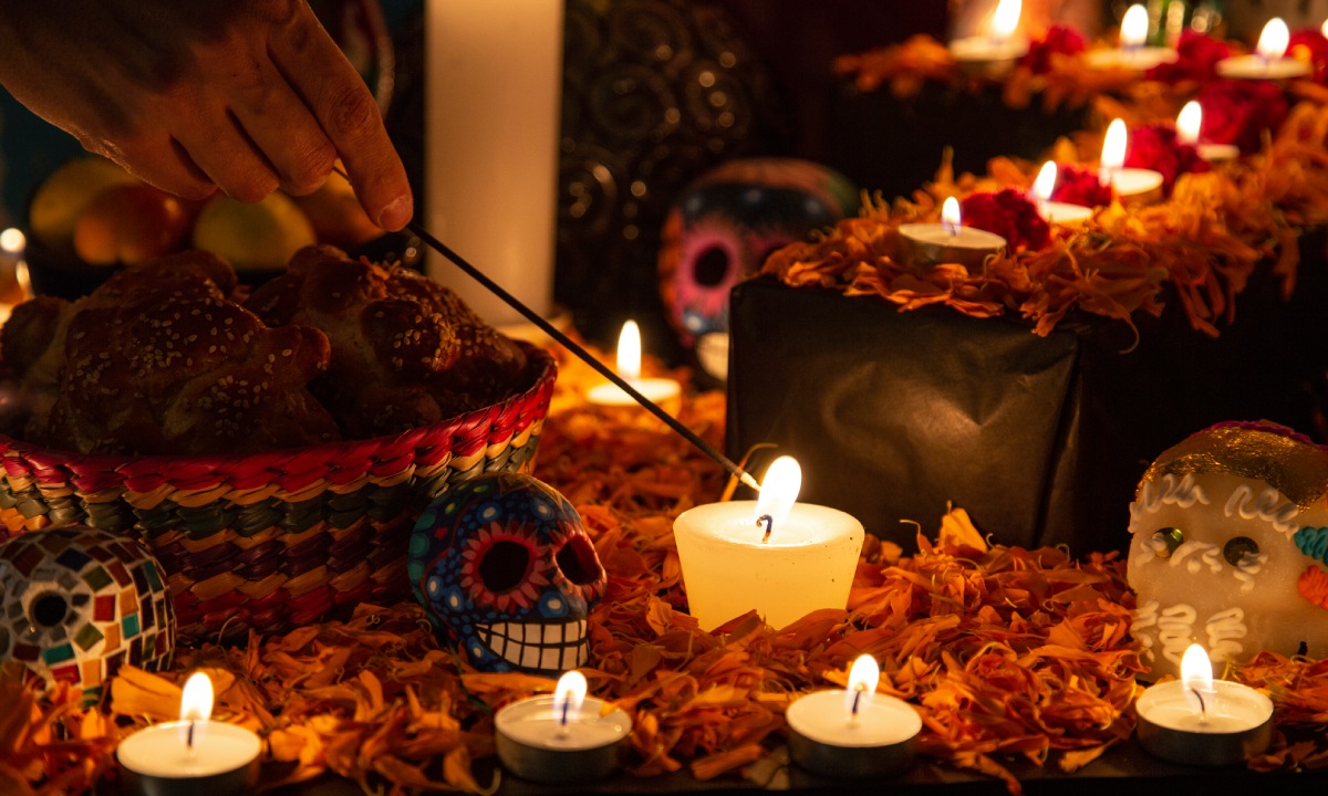 Persona encendiendo vela en altar de Día de los Muertos