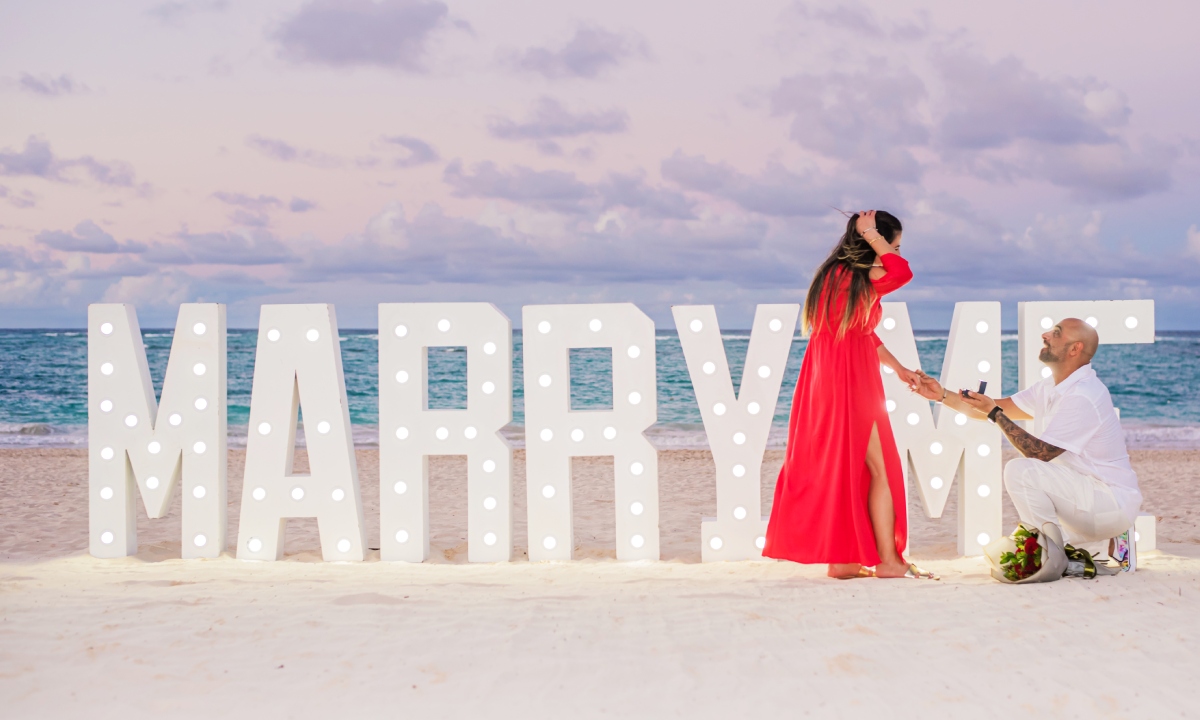 A man proposing in front of an illuminated “Marry Me” sign