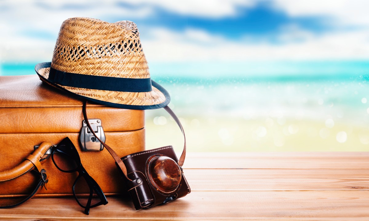 A hat, camera, sunglasses and suitcase on a table