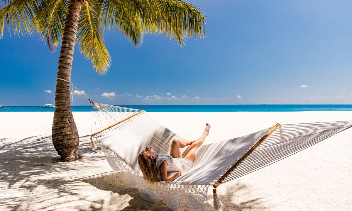 Mujer sobre tumbona junto a palmera en la playa