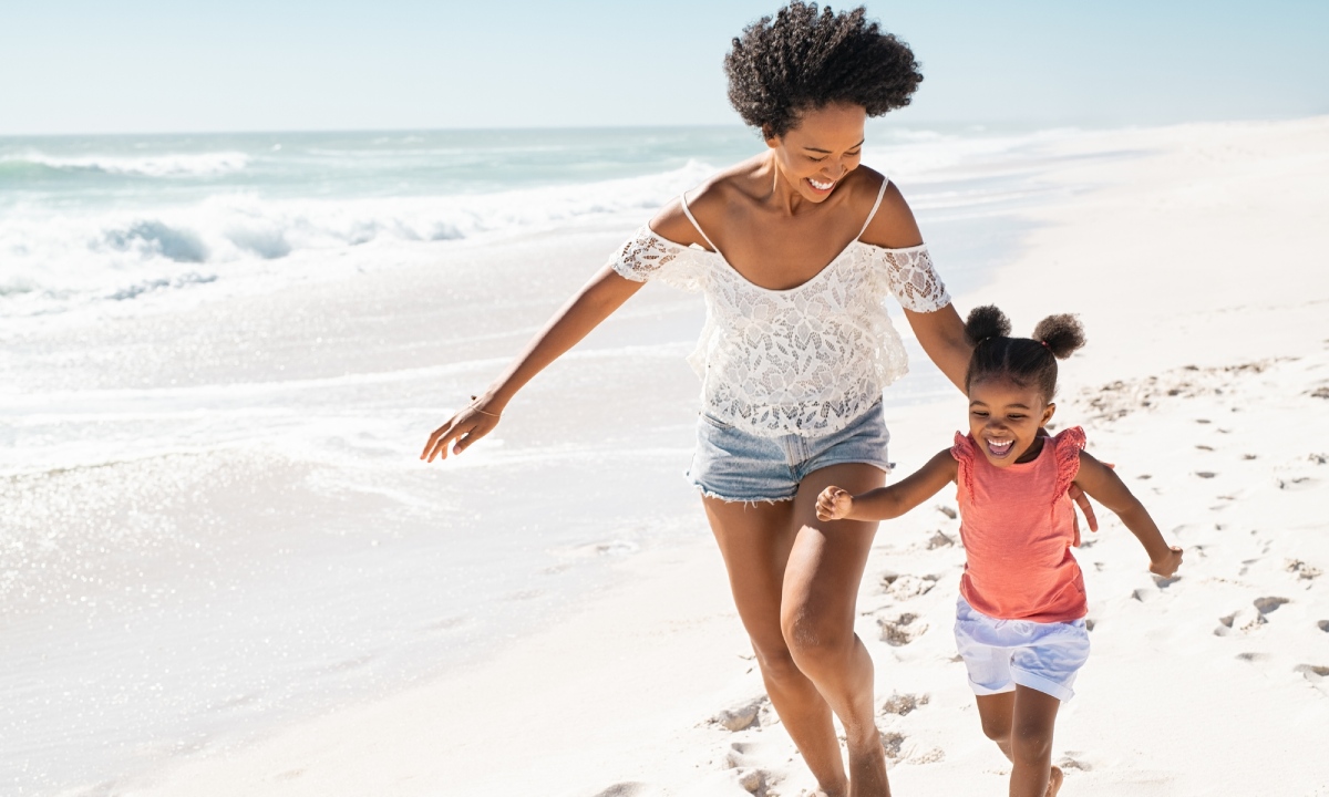 A woman and girl smiling while running along a beach