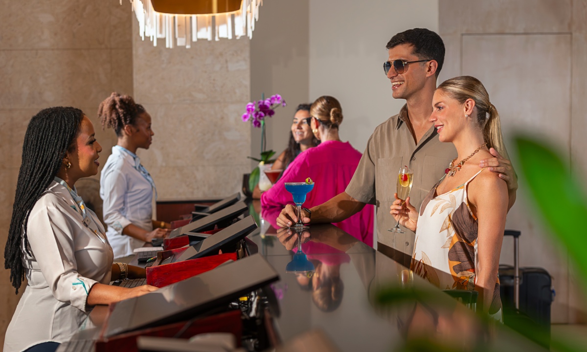 Man and woman with cocktails talking to woman at reception desk