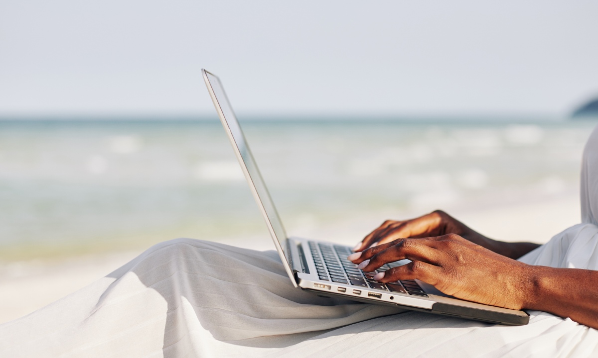 Frau tippt auf einem Laptop am Meer 