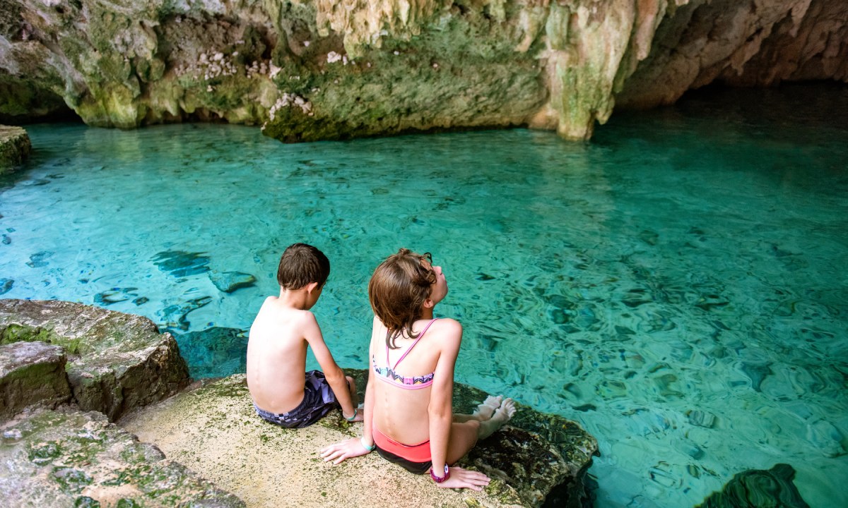 Children sitting on a rock next to a cenote