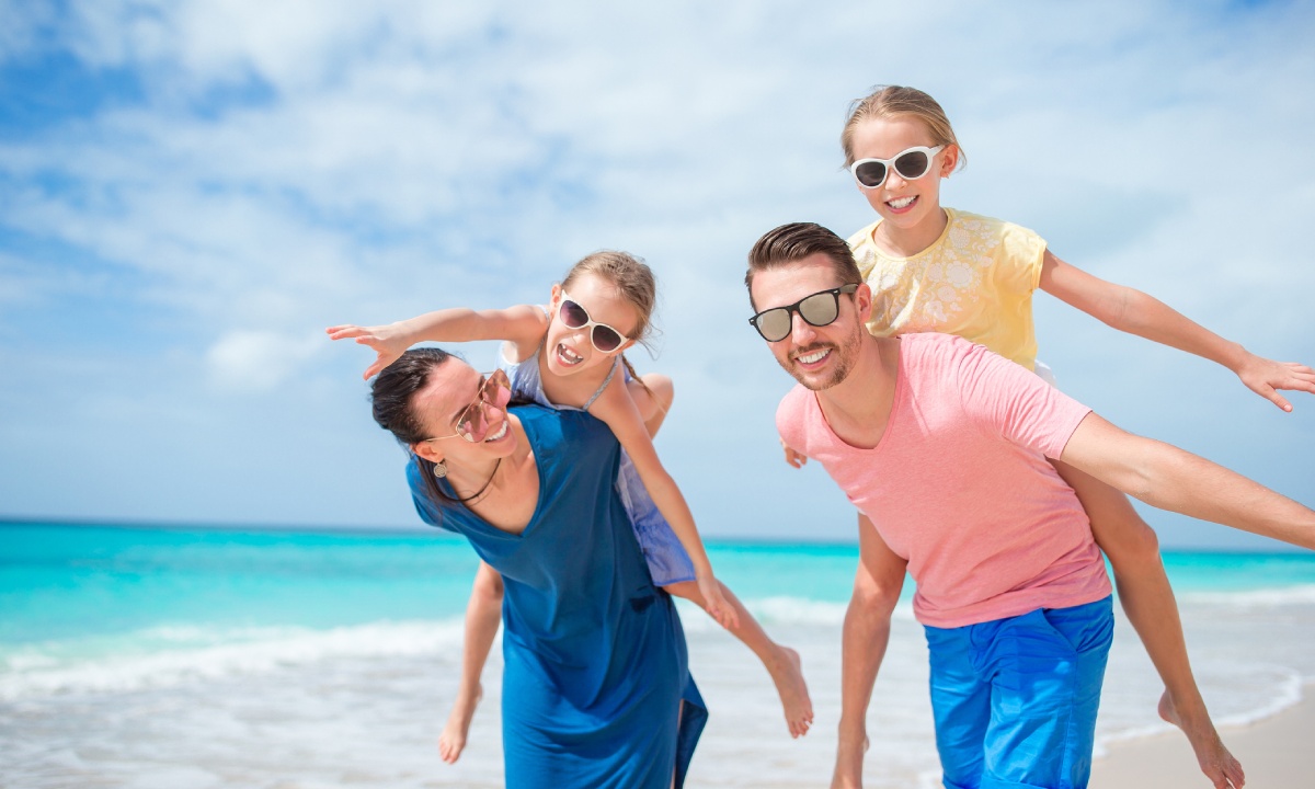 A mum and dad with their daughters riding piggyback on the beach