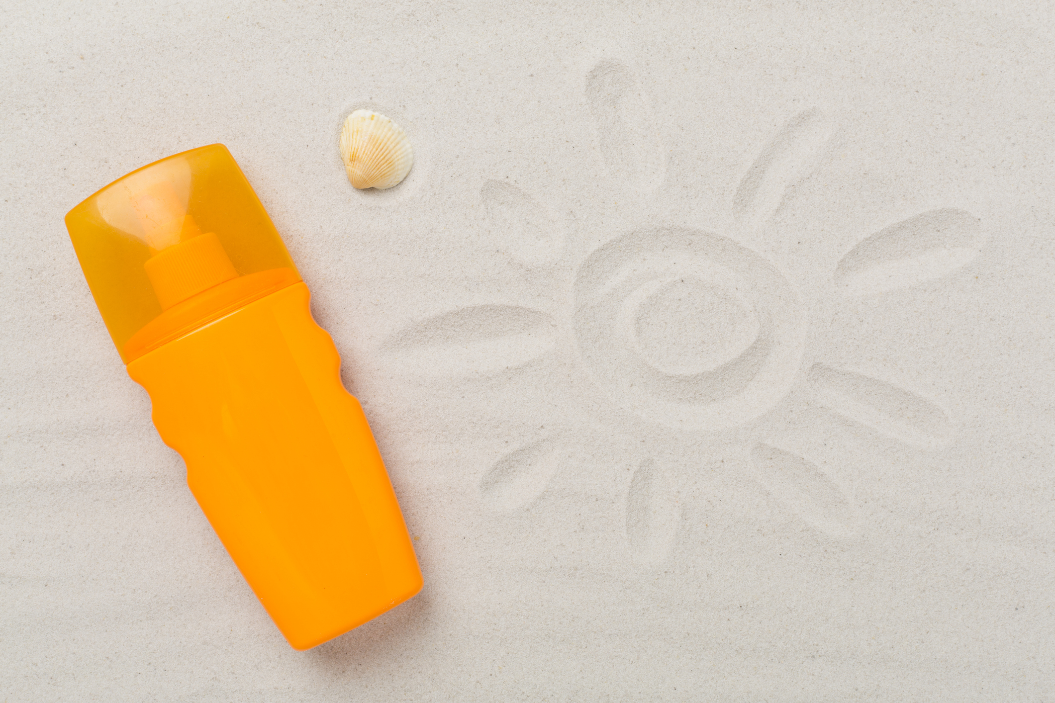 Crema solar junto a dibujo de sol en arena