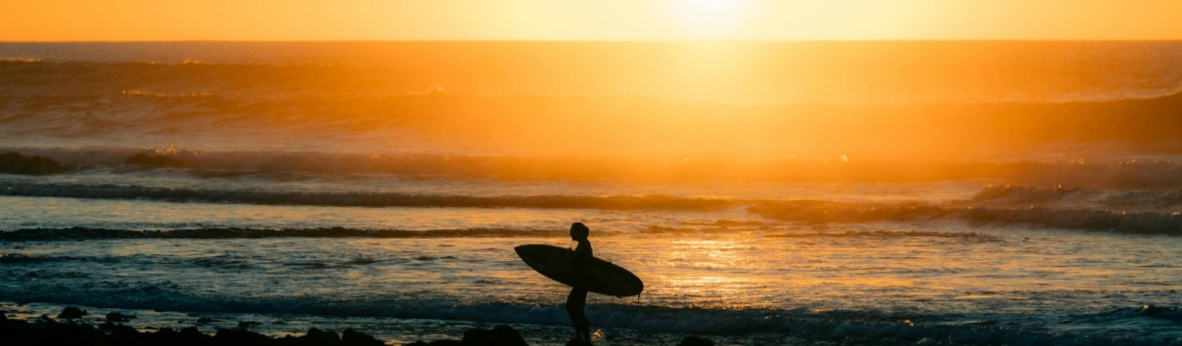 Surfer with their board on the Tenerife coastline at sunset
