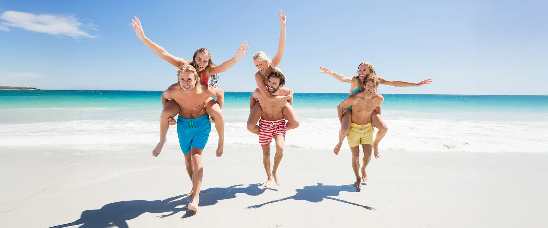 Tres hombres llevando tres mujeres a caballito en playa
