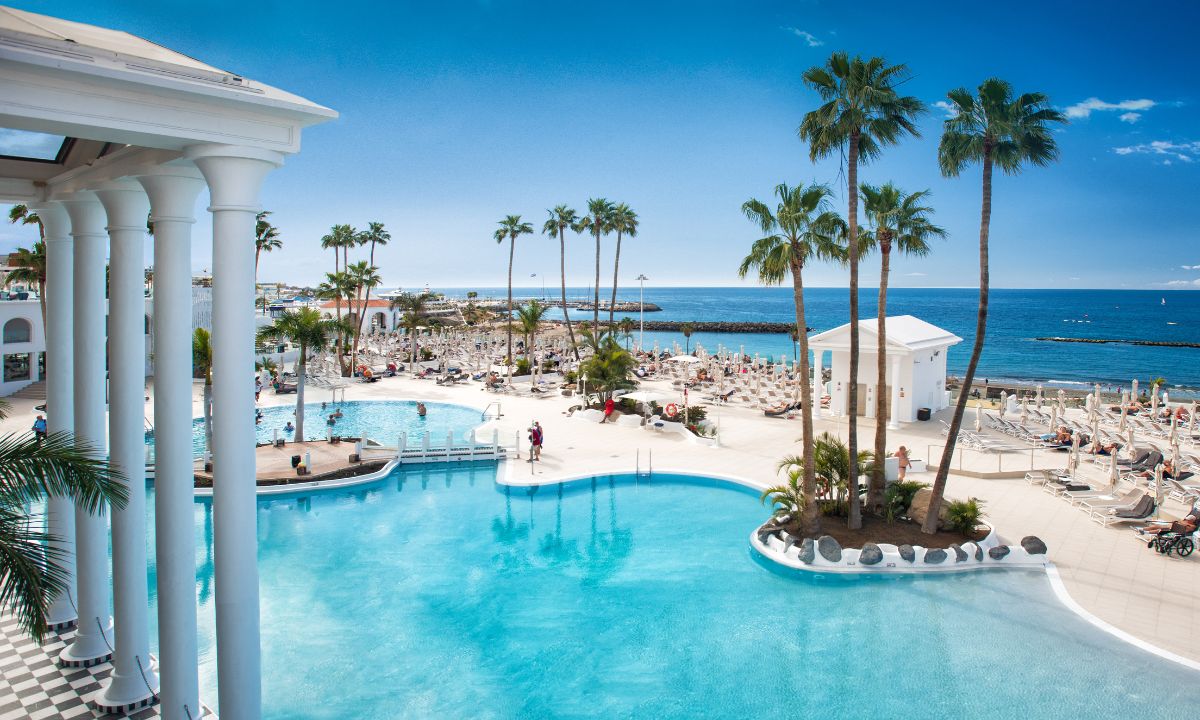 Piscina del hotel Guayarmina Princess en Tenerife con vistas al mar y palmeras bajo el sol.