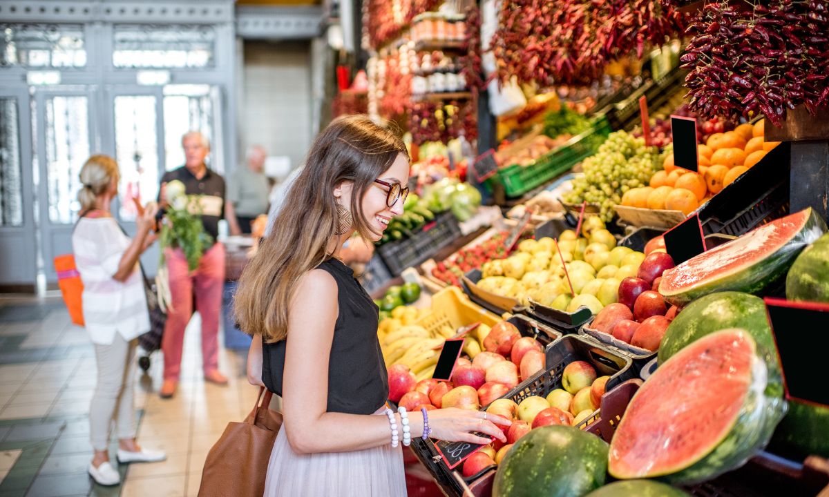 Compradora frente a un puesto repleto de frutas tropicales frescas en un mercadillo.