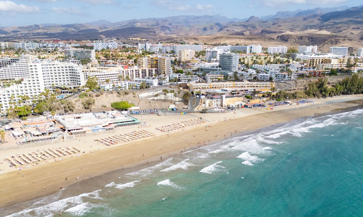 Vista aérea de Playa del Inglés en Gran Canaria con su arena dorada, zonas de hamacas y complejos hoteleros en la costa.