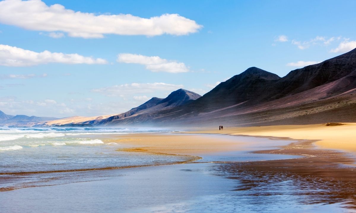 Playa virgen de Cofete en Fuerteventura con montañas de fondo y olas del Océano Atlántico en la orilla.