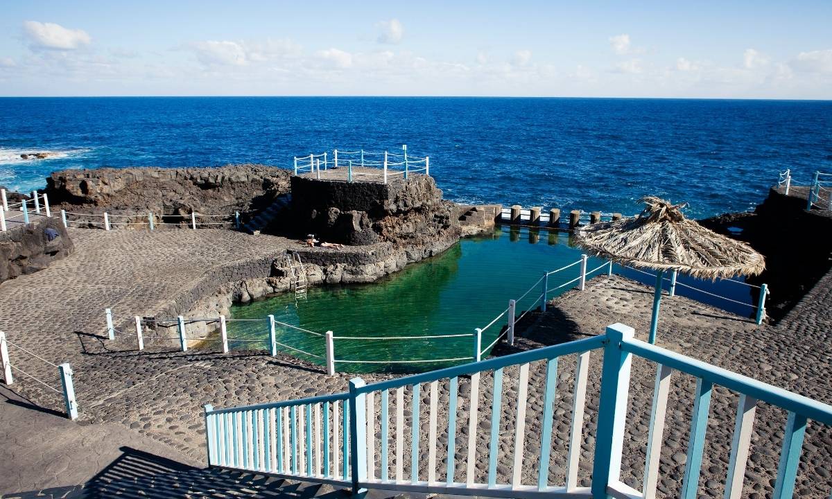 Piscina natural de Charco Azul con sombrillas de paja y agua cristalina en La Palma