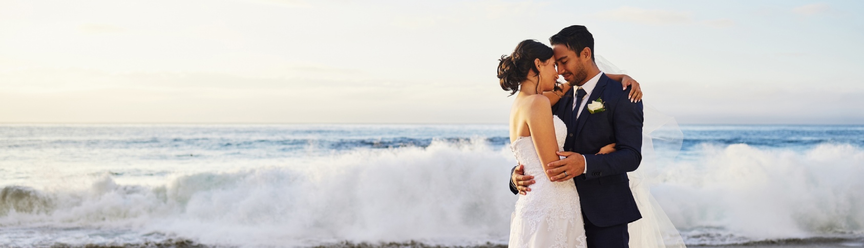Novio y novia abrazados en orilla del mar