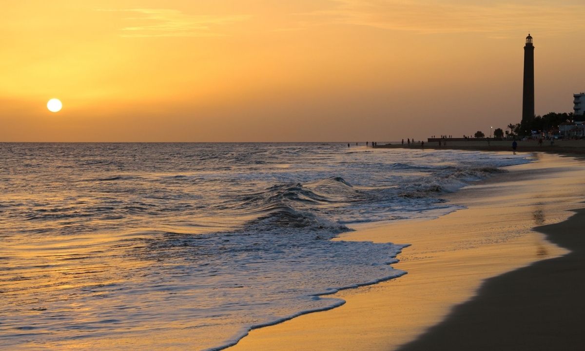 Atardecer dorado sobre la costa y la silueta del Faro de Maspalomas en Gran Canaria.