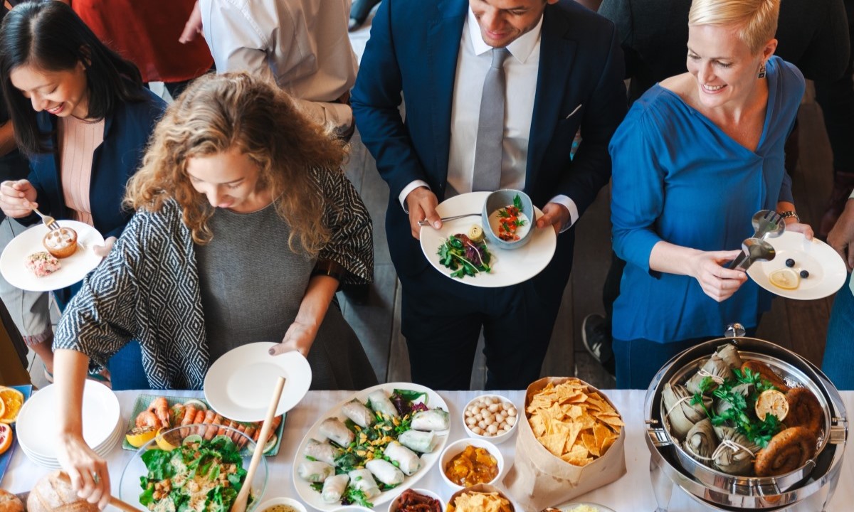 Asistentes a un evento corporativo sirviéndose aperitivos variados de un bufet o catering.