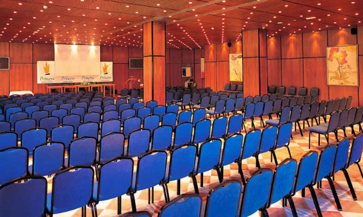 Amplia sala de conferencias en el hotel La Palma Princess con paredes de madera y filas de sillas azules orientadas a un escenario.