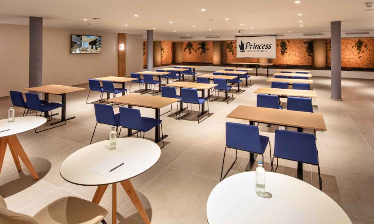Sala de eventos moderna con mesas de madera, sillas azules y una pantalla de proyección al fondo en el hotel Princess Inspire Tenerife.