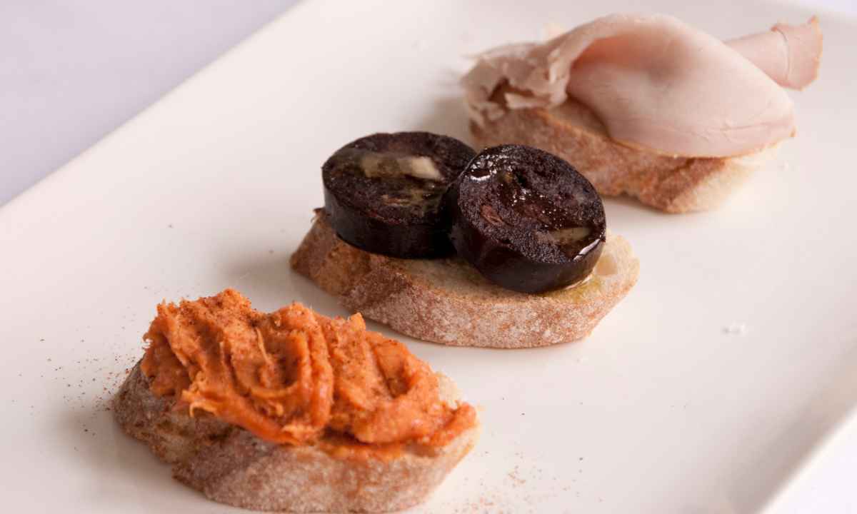 Tres montaditos de pan con paté, morcilla dulce canaria y fiambre servidos en una fuente blanca.
